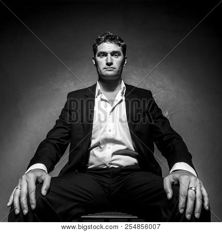 Handsome Man In A Business Suit Sitting On A Chair, Black And White Portrait, Low Angle Shot