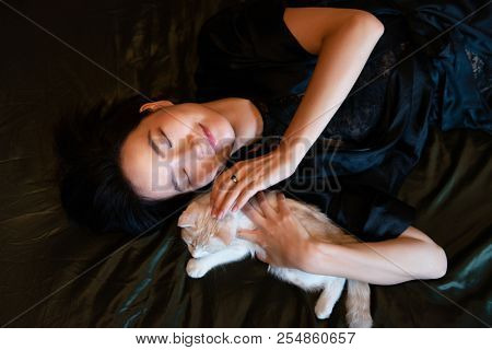 Beautiful chinese young woman wearing pajamas sleeps in bed with her kitten. Lazy morning. Sleppy girl with little kitty in bedroom. Sweet dreams.