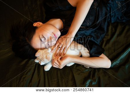 Beautiful chinese young woman wearing pajamas sleeps in bed with her kitten. Lazy morning. Sleppy girl with little kitty in bedroom. Sweet dreams.