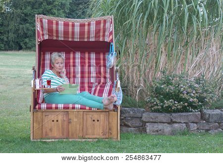 Even On Holiday, The Woman In A Roofed Wicker Beach Chair Must Make An Important Decision