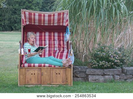 The Book Fascinates The Green Dressed Woman In A Roofed Wicker Beach Chair