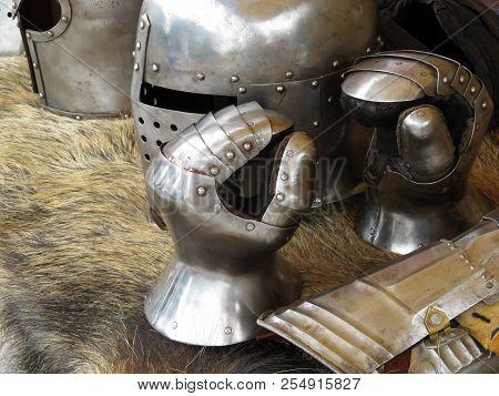 Medieval Helmets And Gloves On A Bearskin Rug. Armor Of Middle Ages, Knightly Equipment, Armory Forg