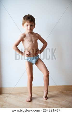 Strong Healthy Little Caucasian Boy In Shorts Showing His Body Muscle Indoors