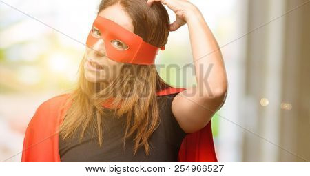 Middle age super hero woman wearing red mask and cape doubt expression, confuse and wonder concept, uncertain future