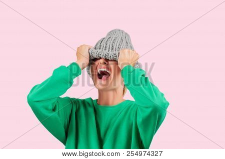 Furious. Emotional Angry Woman Is Pulling Wool Hat Over Her Eyes On Pink Background