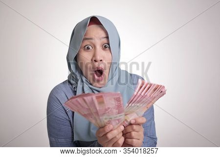 Portrait Of Indonesian Muslim Woman Holding Rupiah Money, Smiling Laughing Winning Gesture