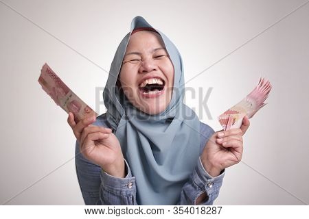 Portrait Of Indonesian Muslim Woman Holding Rupiah Money, Smiling Laughing Winning Gesture