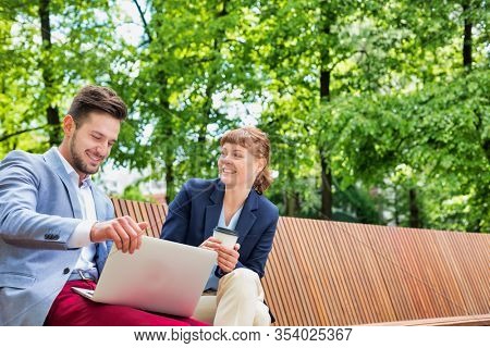 Businessman discussing plans over laptop with beautiful businesswoman while sitting on bench