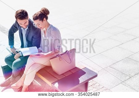 High angle view of businesswoman discussing plans over document with businessman while sitting on bench
