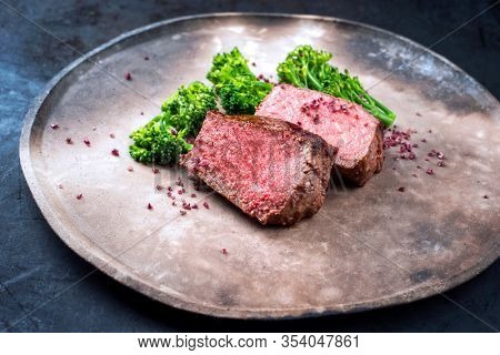 Barbecue dry aged wagyu roast beef natural sliced offered with rapini and salt as closeup on a modern design plate