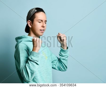 Young Teen Boy In Blue Hoodie Standing, Shouting And Ready To Defend Himself With Fists Over Pastel 