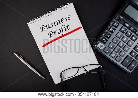 Business Profit Notepad Writing Concept On Dark Background With Pen And Calculator.