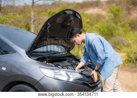 Asian Young Unhappy Man Inspecting Broken Car Engine  In Front Of The Open Hood  Broken Down Car On 