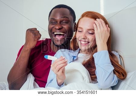 Mixed Race Couple Watching Pregnancy Test In Bed. Redhaired Ginger Woman And Latic Hispanic Afro Man