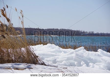 Spring Landscape With A Lake Overgrown With Reeds Near The Coast Covered By White Snow And A Clear S