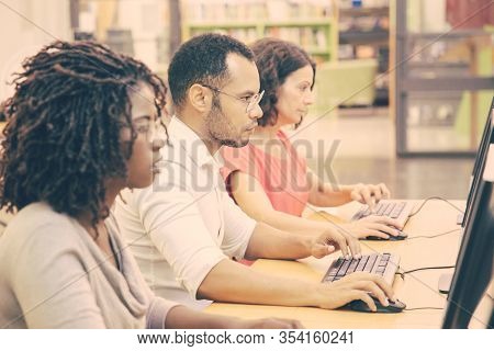 Diverse Group Of Adult Students Working In Computer Class. Line Of Man And Women In Casual Sitting A