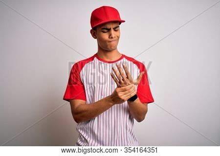 Young handsome african american sportsman wearing striped baseball t-shirt and cap Suffering pain on hands and fingers, arthritis inflammation
