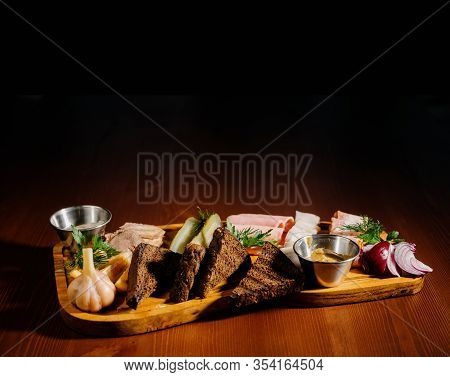 Sliced From Various Types Of Lard, Ham With Sauce And Pickles On A Wooden Board.
