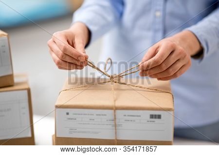 delivery, mail service, people and shipment concept - close up of woman packing parcel box and tying rope at post office