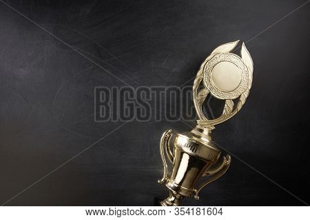 Golden trophy over blackboard background. top view. flat lay.Trophy is a specific achievement, serves as recognition / evidence of merit, awarded for sporting events