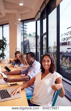 Portrait Of Businesswoman Working At Desk In Shared Open Plan Office Workspace