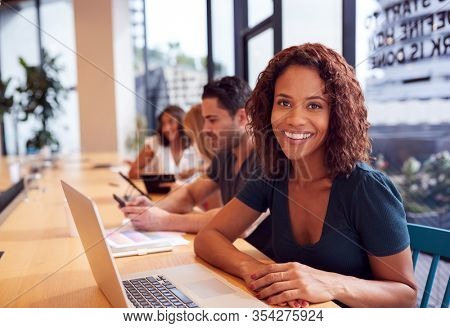 Portrait Of Businesswoman Working At Desk In Shared Open Plan Office Workspace