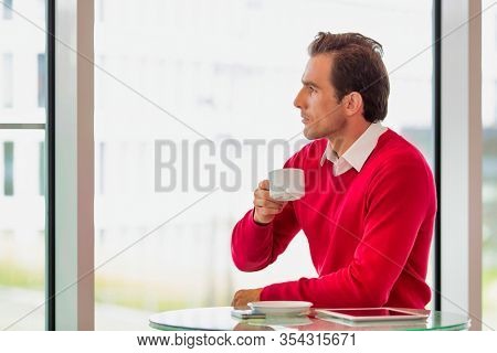 Portrait of thougtful businessman sitting while drinking coffee in lobby