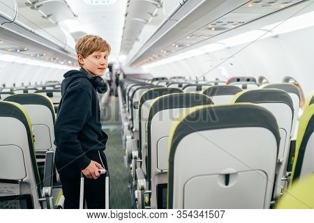 Smiling Blonde Hair Teenager Portrait Staying In Aircraft Corridor With Headphones With Cabin Trolle