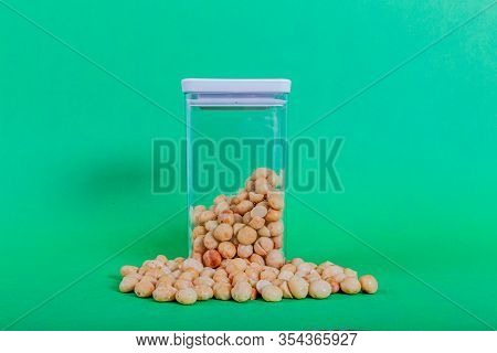 Macadamias Outside And Inside A Transparent Plastic Container With A Green Background, Also Called Q