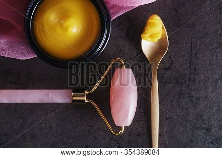 Beautiful Picture Of Golden Solid Skincare Oil In Elegant Black Glass Jar, Golden Spoon And Rose Qua