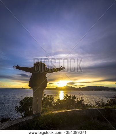 A Young Man With Open Arms At Dawn In The Town Of Fuenterrabia In Winter. Basque Country