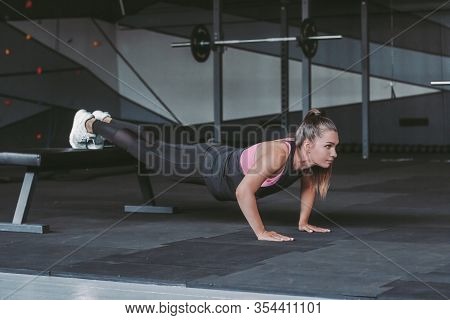 Beautiful Young Determined Sports Woman Doing Push Ups Exercises In Dark Gym. Attractive Muscular Fi