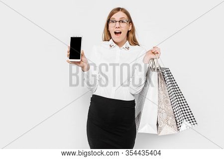 Image Of A Young Pregnant Businesswoman Wearing Glasses, Shows A Blank Smartphone Screen, With Packa