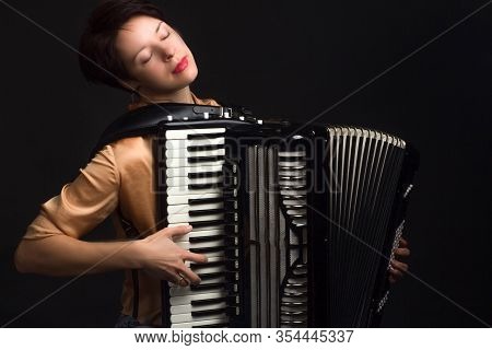 A Brunette In A Gold Shirt, With Short Haircut, On A Dark Kground Of The Studio. Play The Accordion