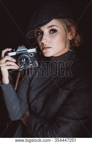 Beautiful Girl Blonde Photographer In A Strict Suit And A Cappie Is Holding An Old Retro Camera In H