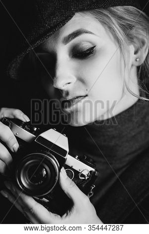 Beautiful Girl Blonde Photographer In A Strict Suit And A Cappie Is Holding An Old Retro Camera In H