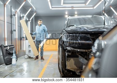 Man Preparing Protective Film For Sticking On A Car Body, Taking It From The Roll At The Vehicle Ser