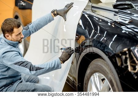 Man Preparing Protective Film For Sticking On A Car Body, Marking It To With A Pen At The Vehicle Se