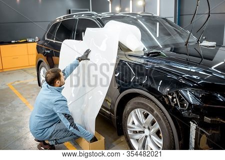 Man Preparing Protective Film For Sticking On A Car Body, Marking It To With A Pen At The Vehicle Se