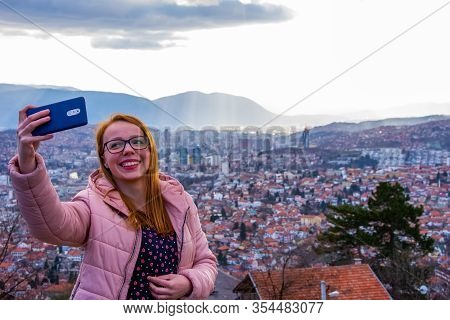 Girl With Glasess And Brown Hair Taking Selfie Above Sarajevo With Mobile Phone