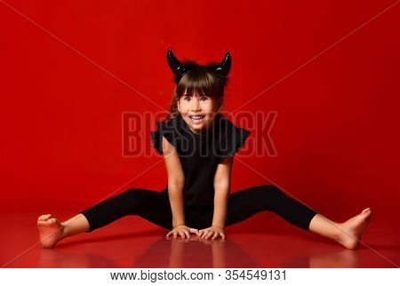 Lovely Brunette Child With Devil Horns, In Black Blouse And Leggings, Barefoot. She Is Smiling While