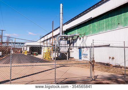 Braddock, Pennsylvania, Usa 3/7/20 A Green And White Industrial Warehouse With A Fenced In Parking A