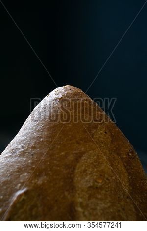 Edge Of Fresh Dark Loaf Of Bread On Black Background. Yeast Product.