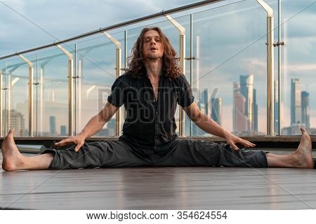 Athletic Sporty Man Doing Straddle Splits Outdoors On Urban Background At Skyscraper Roof. Upavista 
