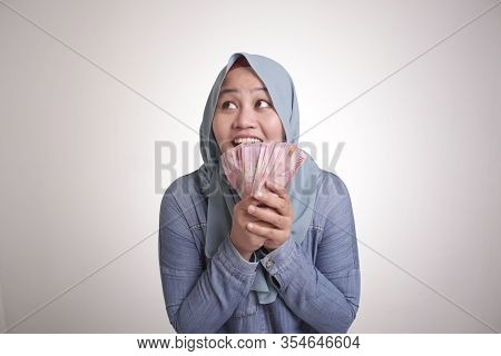 Portrait Of Indonesian Muslim Woman Holding Rupiah Money, Smiling And Thinking Gesture