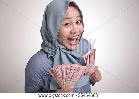 Portrait Of Indonesian Muslim Woman Holding Rupiah Money, Smiling Laughing Winning Gesture