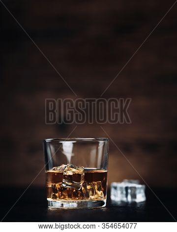 Whisky, Whiskey, Bourbon Or Cognac With Ice Cudes On Black Stone Table And Wood Background