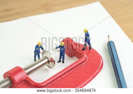 Miniature Worker Working With Red Squeezed Clamp On Notebook With Pencil Using As Budget Or Financia