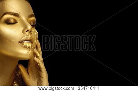 Gold Paint smudges drips from the face lips and hand, lipgloss dripping from sexy lips, golden liquid drops on beautiful model girl's mouth, gold metallic skin make-up. Beauty woman makeup close up