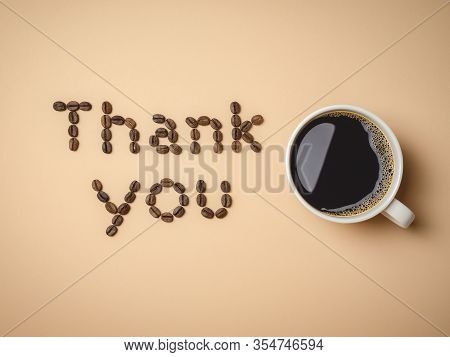 Top View Of Roasted Coffee Beans Arranged In Letters And Hot Coffee In White Coffee Cup On Light Bro